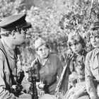 Vier Menschen in Militäruniformen sitzen im Gespräch zusammen, umgeben von Büschen.