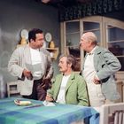 Drei Männer in einem Raum; der sitzende Mann trägt ein T-Shirt mit dem Wort "TAVARAT". Sie wirken in ein Gespräch vertieft.