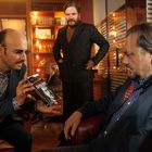 Ein Mann hält ein Buch mit dem Titel "Ziemlich beste Feinde" und einem Schwarz-Weiß-Porträt. Drei Männer in einer Büroumgebung.