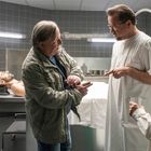 Im Raum eines Leichenschauhauses diskutieren zwei Männer, während eine Frau zuhört. Ein Körper liegt auf dem Tisch.