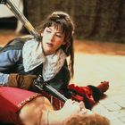 Zwei Frauen in historischer Kleidung. Die stehende Frau hält ein Gewehr auf eine am Boden liegende Frau.