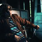 Ein Jugendlicher mit Sonnenbrille lehnt lässig auf einem Fahrrad in einem schattigen, verlassenen Raum.