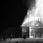 Ich kann die Texte nicht lesen. Eine Scheune steht in Flammen, Menschen rennen mit Geräten, um das Feuer zu löschen.