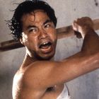 Ein Mann mit verschwitztem Gesicht hebt einen Holzstab, zeigt einen entschlossenen und emotionalen Ausdruck.