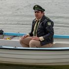 Ein Mann in Polizeiuniform sitzt in einem Ruderboot auf dem Wasser.