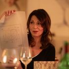 Eine Frau hält ein Blatt mit einer Herzzeichnung und technischen Details. Die Umgebung ist warm mit Kerzenschein.