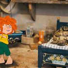 Eine Illustration: Ein rothaariger, animierter Junge mit verschränkten Armen steht neben einem Bett, auf dem eine Schildkröte liegt.