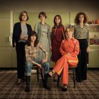 Sechs Frauen posieren in einem Raum mit grünen Küchenschränken, zwei sitzen, vier stehen. Vintage-Stil.