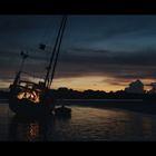 Ein Segelboot liegt schräg im Wasser am Strand. Der Himmel zeigt ein farbenprächtiges Abendrot.
