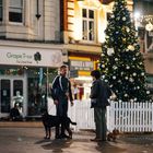 "Text: Grape Tree, Molded & Vapes. Zwei Männer mit Hunden stehen neben einem geschmückten Weihnachtsbaum auf einer Straße."