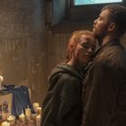 Eine Person in gemustertem Anzug mit Tasche steht in einem beleuchteten Flur.