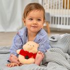 Ein kleines Kind sitzt auf einer grauen Decke und hält ein Plüschtier. Im Hintergrund steht ein weißes Kinderbett.