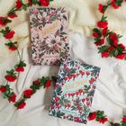 "TWILIGHT" und "NEW MOON" auf floral verzierten Buchcovern, umgeben von roten Rosen und einem beigen Stoff.