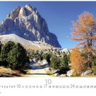 "Dolomiten", "10", "CASARES EDITION". Berglandschaft mit steinigem Pfad, grünen und herbstlichen Bäumen unter klarem Himmel.