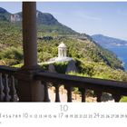 "Son Morroig", Monatsübersicht darunter. Blick auf ein blaues Meer, grüne Hügel und eine klassische weiße Säulenstruktur.