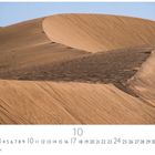 "Sahara", darunter eine Kalenderseite des Monats Oktober. Eine große, geschwungene Sanddüne unter blauem Himmel.