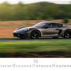 „Porsche Cayman“, „CASARES EDITION“. Ein grauer Sportwagen fährt schnell auf einer Straße mit verschwommenem Hintergrund.