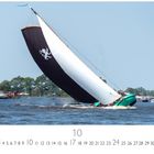 Eine große Segelboot-Regatta mit einem schwarzen Segel, auf dem ein weißer Löwe abgebildet ist. Unten Monatskalender Oktober.