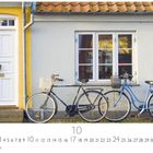 "Straßenidylle" über einem gelben Haus mit weißer Tür und zwei Fahrrädern davor. Darunter Kalenderdatum.