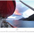 Text: "Fjordansicht mit Schiff". Ein rotes Rettungsboot hängt an einem Schiff. Rechts Berge und ein ruhiger Ozean bei Sonnenuntergang.