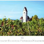 "Kirche in Hagnau." Ein Kirchturm ragt über ein grünes Weinfeld, blauer Himmel im Hintergrund.