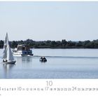 Kalenderblatt für Oktober, am Altmühlsee. Boote auf ruhigem Wasser, umgeben von grüner Vegetation.