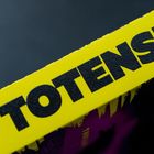 Gelber Hintergrund mit schwarzem Text "TOTEN". Darunter dunkles, abstraktes Muster in Violett und Schwarz.