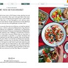 NENI AM NASCHMARKT mit orientalischen Gerichten. Sichtbar: Shakshuka, Brot, Salat, ein Bagel und ein Glas Tee auf rotem Tisch.