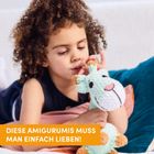 Text: "DIESE AMIGURUMIS MUSS MAN EINFACH LIEBEN!" Ein Kind hält ein gestricktes Stofftier und sieht es liebevoll an.