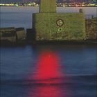 „3nds, 5kts“ auf einem Schild an einem Leuchtturm in den Abendstunden, Spiegelung des roten Lichts im Wasser.