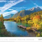 Text: "OKTOBER". Landschaft mit See, Steg und bunten Herbstbäumen, umrahmt von Bergen unter blauem Himmel mit Wolken.