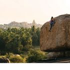 „A beautiful warm-up boulder with the best backdrop of the classic Hampi temples in the background, India.”  
Eine Person erklimmt einen großen Felsen, im Hintergrund Palmen und Tempel.