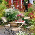 10, 2021. Blumengarten mit Holzmöbeln, kleinem Haus mit Kletterpflanzen und Vogelhäuschen.