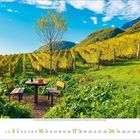 Tisch mit Wein und Gläsern; umgeben von Weinreben im Herbst; blauer Himmel, Berge im Hintergrund. Kalender für Oktober 2024.