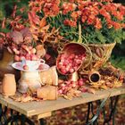 Herbstliche Szene: Ein Tisch mit buntem Herbstlaub, kleinen roten Äpfeln in einem Korb und Chrysanthemen.
