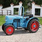 Das Wort „Eicher“ ist auf einem hellblauen Traktor mit roten Rädern zu sehen. Im Hintergrund eine weiße Mauer.