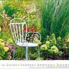 Text enthält eine Monatsübersicht von Oktober 2023 auf einem Kalender. Ein weißer Gartenstuhl steht inmitten bunter Blumen und Gräser.