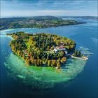 Ein bewaldetes Eiland im klaren Wasser, mit Gebäuden und Anlegestellen, umgeben von einer größeren Wasserfläche.
