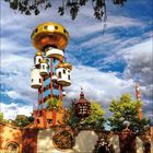 Eine fantasievolle Turmkonstruktion aus goldenen und weißen Elementen, umgeben von Bäumen und einem dramatischen Himmel.