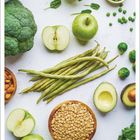 "Oktober" unten. Verschiedenes grünes Gemüse und Obst: Äpfel, Brokkoli, Bohnen, Erbsen, Avocado und Linsen in Schalen.