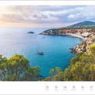 „Küste von Ibiza, Spanien“. Juli, Woche 28. Ein Segelboot im blauen Meer vor einer von Bäumen gesäumten Felsküste.