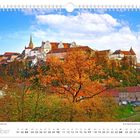 Oktoberkalender mit herbstlicher Ortenburg. Datum von 01 bis 31. Blauer Himmel, historische Gebäude, orangefarbene Bäume.