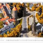 "Oktober" steht am unteren Rand. Luftaufnahme einer Stadt mit Donatsturm und Jakobikirche, umgeben von herbstlichen Bäumen.