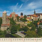 Kalender unten: Oktober 2023. Ansicht einer historischen Stadt mit Türmen und roten Dächern, umgeben von viel Grün.
