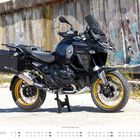 Zu sehen ist ein Motorrad BMW R 1300 GS, Baujahr 2024. Es steht vor einer graffiti-bedeckten Betonwand. Text: „OKTOBER“.