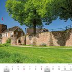 Stadtmauer und Mühlenturm in Rees. Roter Turm, weißes Haus, grüne Wiese, großer Baum, blauer Himmel; unten Kalender Mai 2027.
