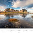 Kalender für Oktober: Vestrahorn, Stokksnes, Höfn. Berge spiegeln sich im Wasser unter blauem Himmel, umgeben von Gras.