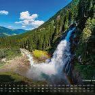 Kalender mit Krimmler Wasserfällen im Vordergrund, umgeben von Wald, unter blauem Himmel und weißen Wolken.