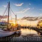 Fischerhafen Bremerhaven. Ein Sonnenuntergang spiegelt sich im Hafen, Boote und moderne Gebäude säumen das Wasser.