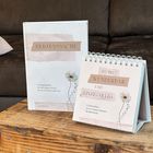 "HERZENSSACHE" und "DU BIST WUNDERBAR UND EINZIGARTIG" auf Buch und Kalender mit Blumenmotiven vor braunem Sofa.